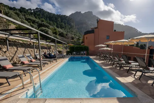 Outdoor pool surrounded by reclining chairs and an orange building in the background