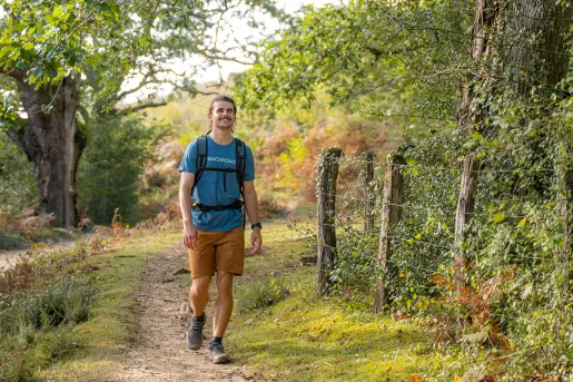 Man walking through a trail in a forest, looking up towards the sky