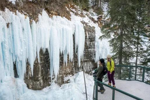 Two women standing on a balcony looking at large, frozen waterfalls