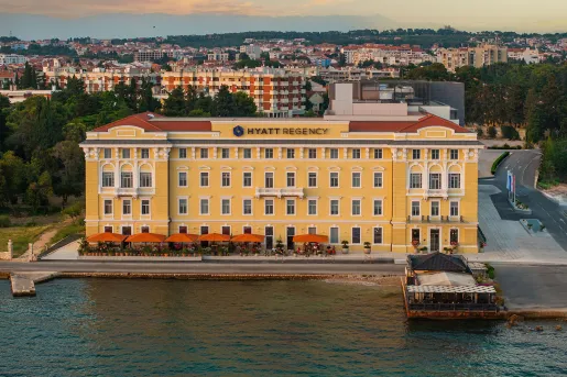 Exterior view of large, yellow and beige hotel building with the ocean in front