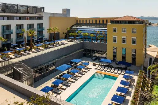 Exterior view of yellow and white hotel building with an outdoor pool and blue chairs