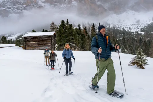 Group of hikers walking through a snowy valley with a wooden cabin in the back