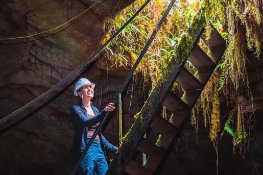 Woman wearing a hardhat, climbing a ladder in a cave