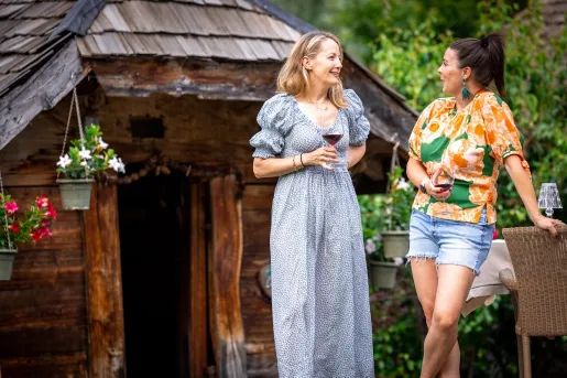Two women standing in front of a cottage, drinking wine