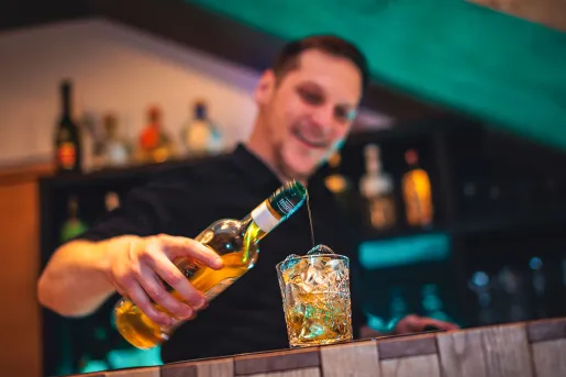 Male bartender pouring alcohol into a glass filled with ice