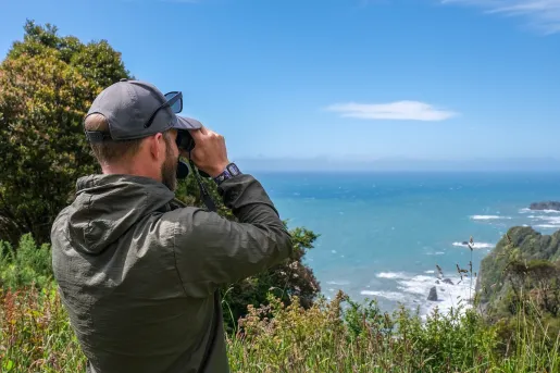 Man using binoculars to look past a cliff towards the ocean