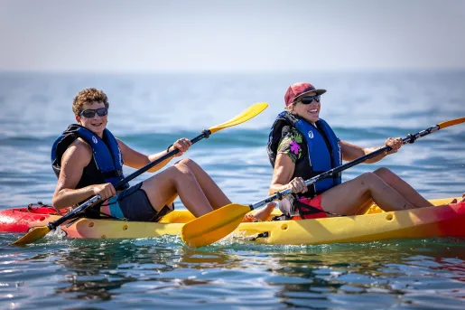 Man and woman smiling while paddling on a yellow and red kayak