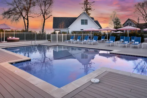 Outdoor pool with the sunset in the background and a large, white house