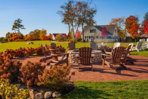 Large lawn area with wooden chairs surrounding a large, stone firepit