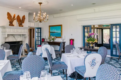 Restaurant with white table cloths over square tables, with blue and white chairs