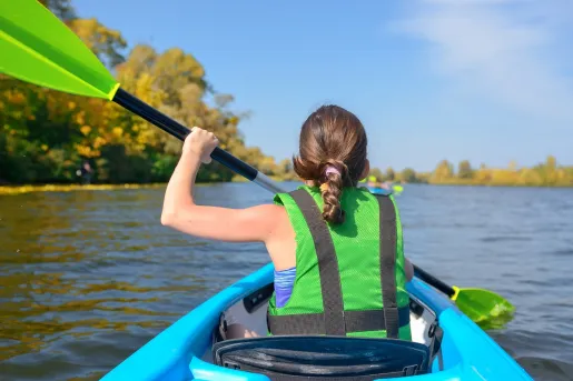 Girl paddling on a blue kayak, while wearing a green life vest
