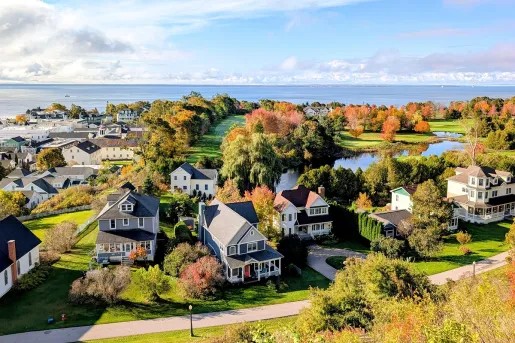 A town with tall trees and white houses, with the ocean in the distance