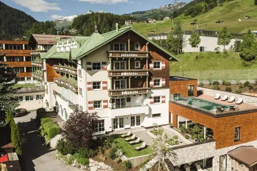 Exterior view of white, brown and green hotel building, with a grassy valley in the background