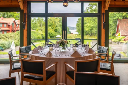 Large, wooden circular table with black cushioned chairs, with a large lawn in the background