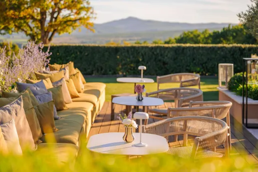 Terrace dining area at Hôtel La Bastide Saint Georges, featuring modern outdoor sofas and woven chairs set against a scenic, hilly landscape.