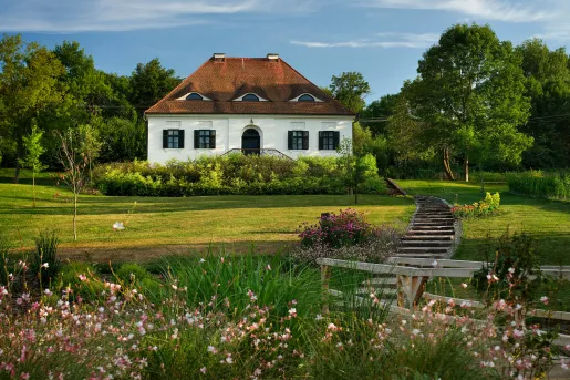 Exterior view of white and red cottage with a garden and grass field in front
