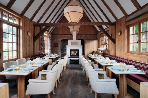 Restaurant with white, cushioned chairs surrounding wooden dining tables