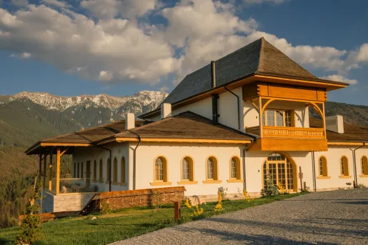Exterior view of a large white and brown building in a valley, being hit by the sunlight