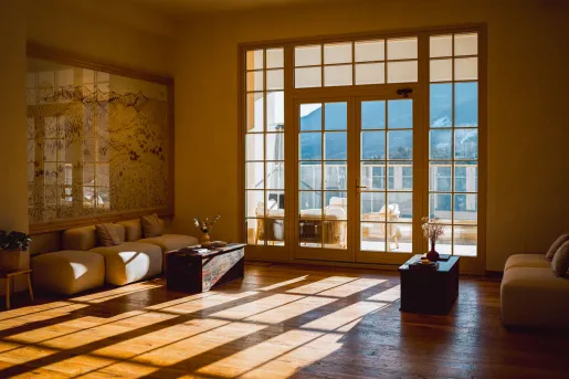 Room with large windows and the sunlight coming through, with large mountains outside