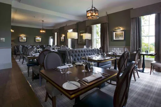 Restaurant with dark wooden tables and black chairs, with tall windows along the walls