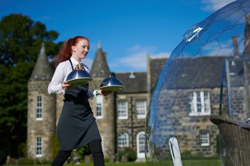 Waitress holding two plates of food walking in front of a castle-styled building