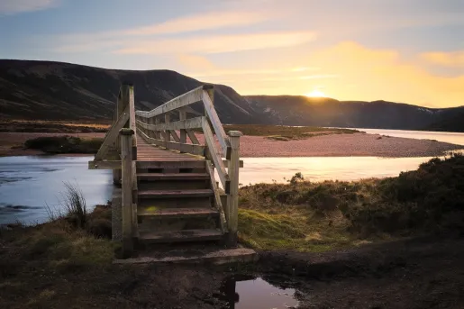 Wooden  bridge over a small river, leading to a hill