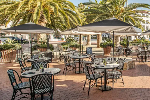 The outdoor patio seating of the restaurant at Hotel Californian in Santa Barbara, CA featuring black and white bistro chairs and black umbrellas.