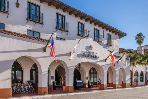 The Hotel Californian in Santa Barbara, featuring Spanish Colonial architecture with a white colored building, arches and flags hanging on the front.