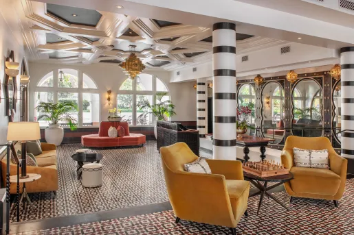 The lobby of the Hotel Californian features Moroccan-inspired geometric ceiling details, yellow velvet chairs, and black-and-white striped columns.