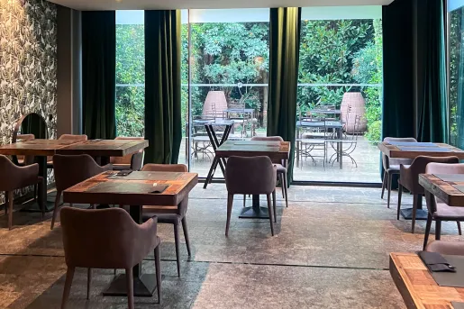 Hotel restaurant with wooden dining tables and chairs, with large windows in the back