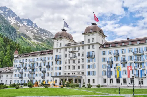 Exterior of the Grand Hotel des Bains Kempinski St. Moritz in Switzerland, featuring a large grand white building with light blue window shutters.