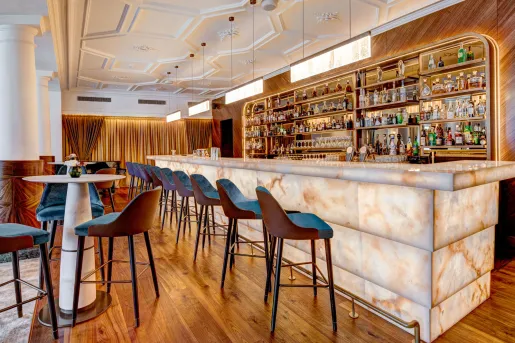 The lobby bar (Quintessence Bar & Lounge) at the Grand Hotel des Bains Kempinski St. Moritz in Switzerland that features a backlit onyx bar, wood-paneled accents and high-backed modern bar stools.