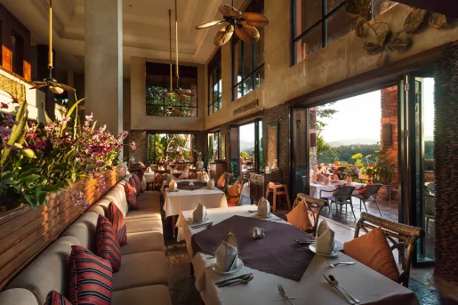 Restaurant with cushioned sofas and white dining tables, with large windows to the right