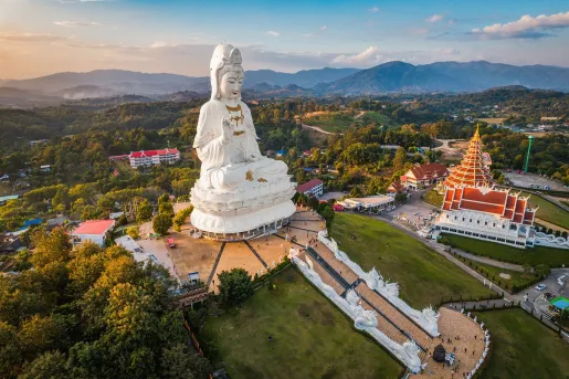 White Buddhist statue at the top of a hill with a town in the background