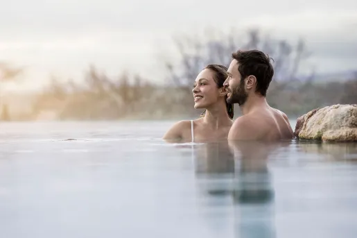 Man and woman in a pool, with the sunset in the background