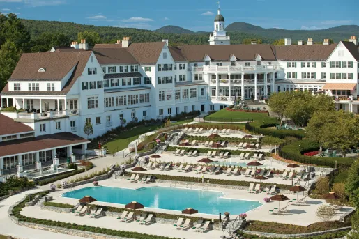 Exterior view of long, white, multi-story hotel building with an outdoor pool in front