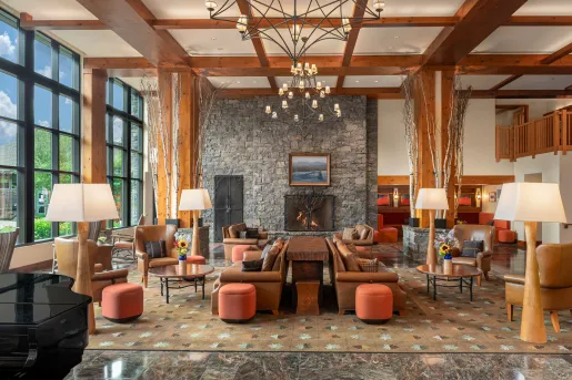 The rustic and grand lobby of The Lodge at Spruce Peak in Stowe, Vermont, featuring soaring timber-frame ceilings and a massive stone fireplace.