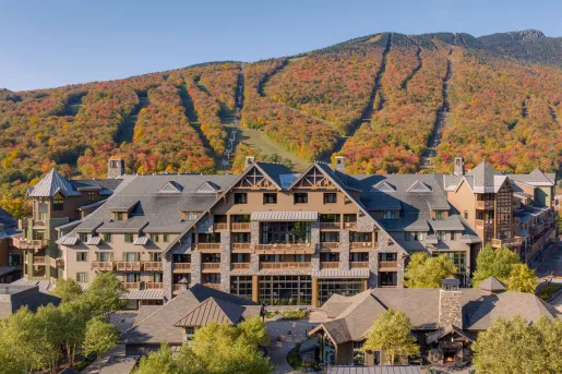 The Lodge at Spruce Peak, a luxury alpine-style resort in Stowe, Vermont, framed by vibrant autumn foliage on the surrounding mountains.