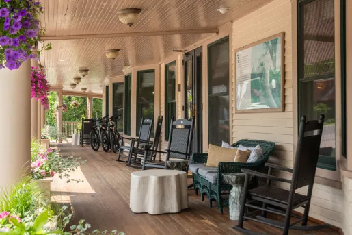 The covered front porch of The Wentworth Inn, featuring rocking chairs, couches and hanging floral baskets