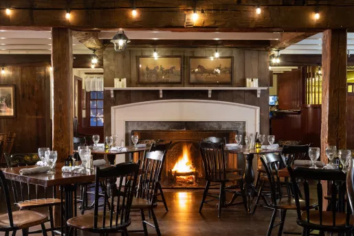 Restaurant dining area with dark brown chairs and tables in front of a lit fireplace