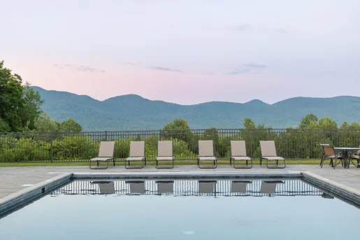 Outdoor pool surrounded by chairs and the sunset in the background