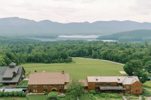 Sky view of two large, brown buildings facing a large forest