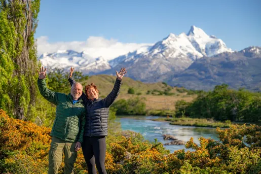 Man and woman smiling with their hands in the air, with a lake in the background