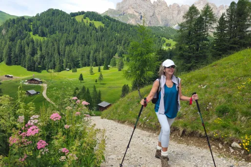 A Backroads guest on a hike in the Dolomites, surrounded by lush green trees and pink flowers.