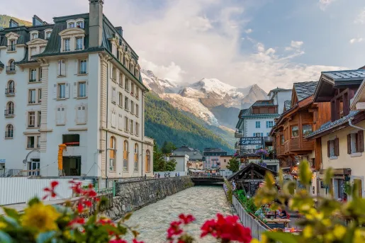 Exterior view of large white building next to a river, with snowy mountains in the distance