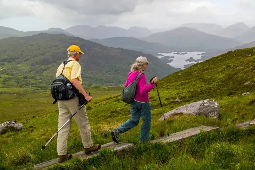 Older couple with hiking poles, walking on a grassy valley