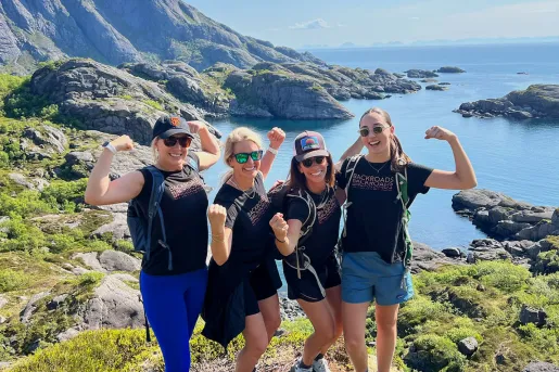 Four women standing on a cliff, flexing their muscles