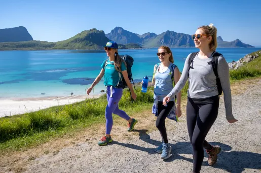 Three women walking on a dirt trail with a large lake in the background