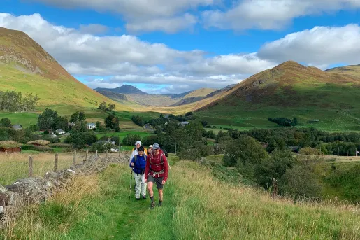 Group of people hiking through a grassy field, with views of large hills in the distance
