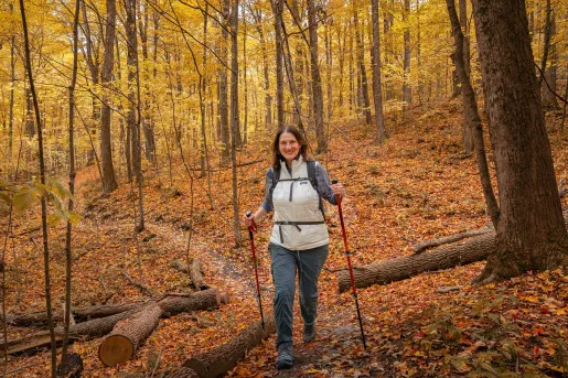 Woman smiling while hiking in a forest, with orange leaves and trees